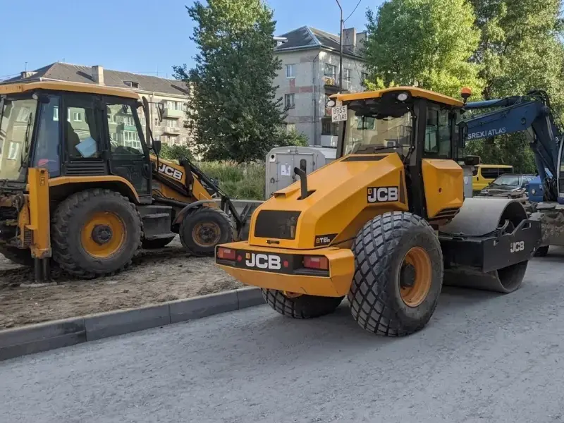 Żółty walec drogowy oraz koparka gąsienicowa JCB na placu budowy – osprzęt i części zamienne do maszyn budowlanych BREMAT.